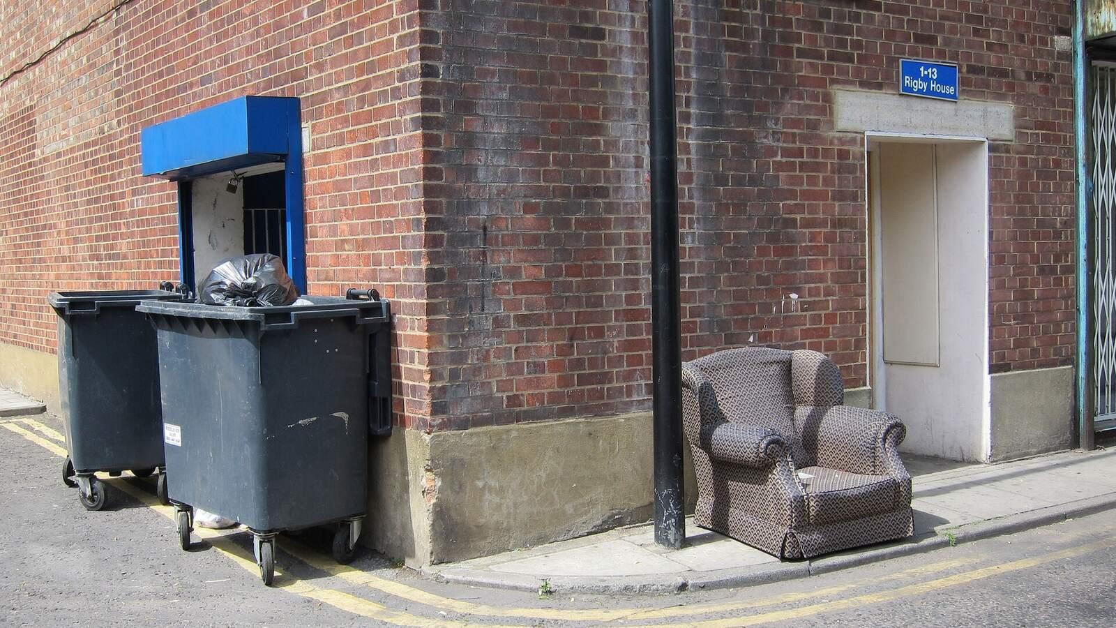 Fauteuil abandonné sur le trottoir à côté de grands conteneurs à ordures, au coin d'une rue