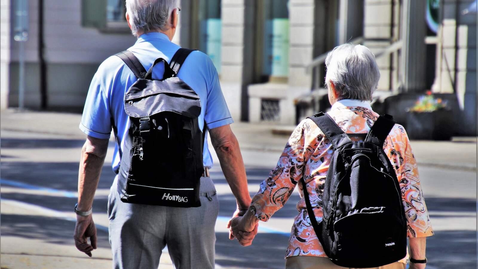 Couple de retraités vu de dos, main dans la main, sac à dos sur l'épaule