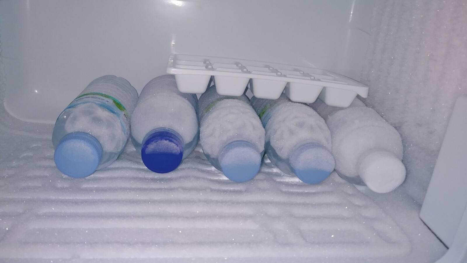 Bouteilles d'eau gelées et bac à glaçons rangés dans le congélateur d'un réfrigérateur