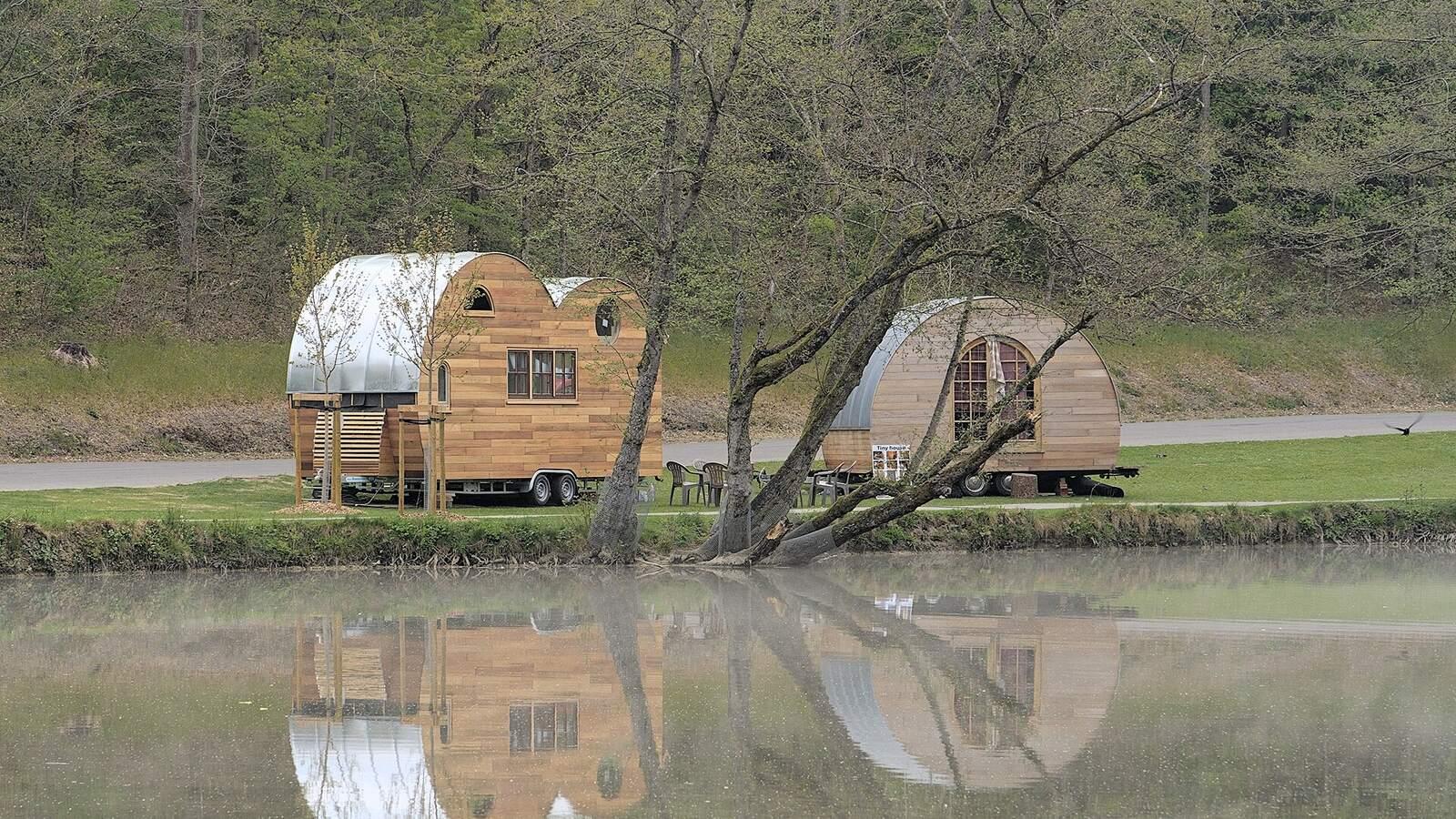 Deux tiny houses à bardage bois posées au bord d'un étang, entourées d'arbres