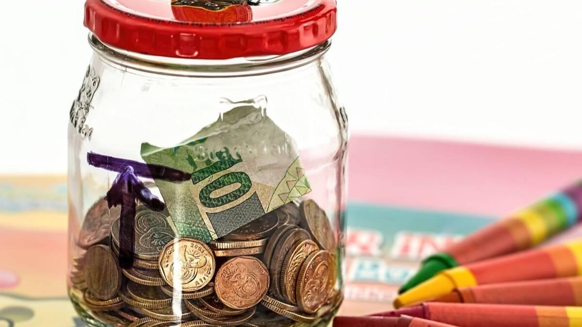 Bocal en verre rempli de pièces de monnaie et d'un billet, à côté de crayons de couleur